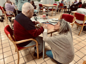Un résident prend son repas dans le réfectoire. Une aide soignante est à ses côtés.