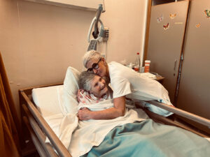 Une infirmière prend dans ses bras une résidente alitée qui sourit.